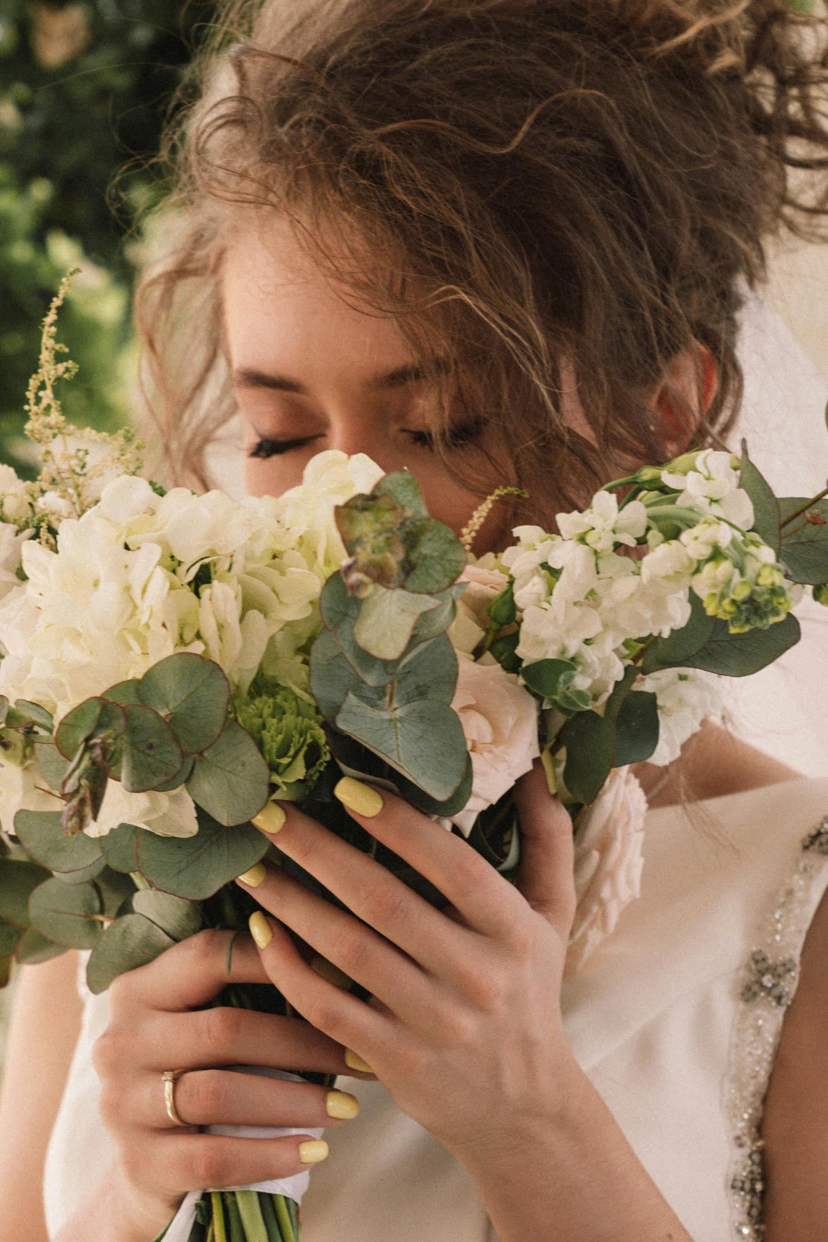 A bride enjoys the scent of her elegant bridal bouquet in a natural setting.