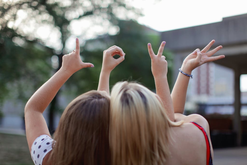 Two young women forming the word 'LOVE' with hand signs, symbolizing friendship in a summer setting.