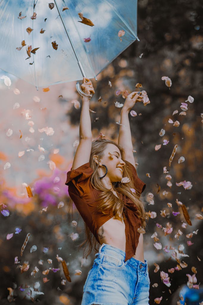 A cheerful woman under an umbrella surrounded by falling flowers, embracing joy and freedom outdoors.