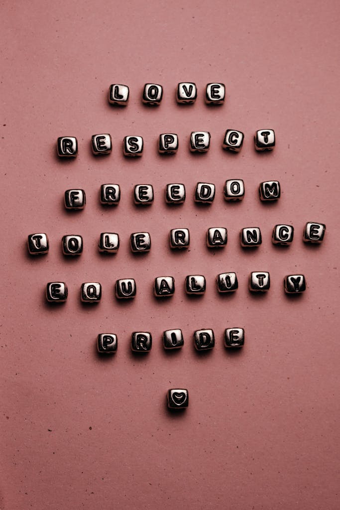 Letter beads forming inspiring words on a pink surface, promoting love, respect, and equality.